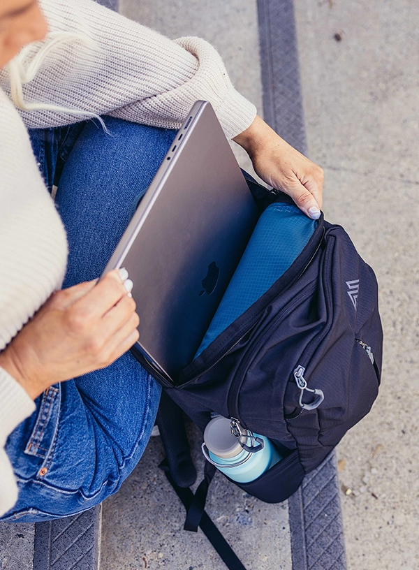 Jaki plecak na laptopa? Kobieta wkłądająca laptop do plecaka.